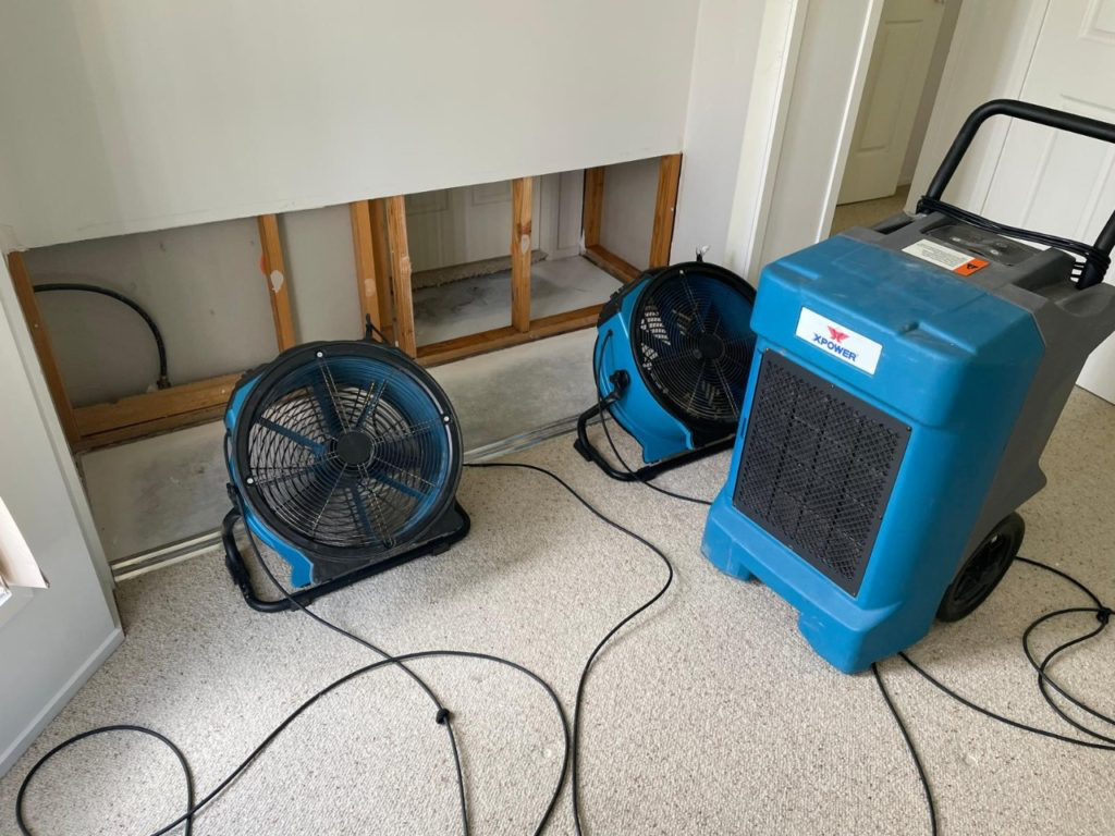 Air movers and a dehumidifier drying a stripped wall